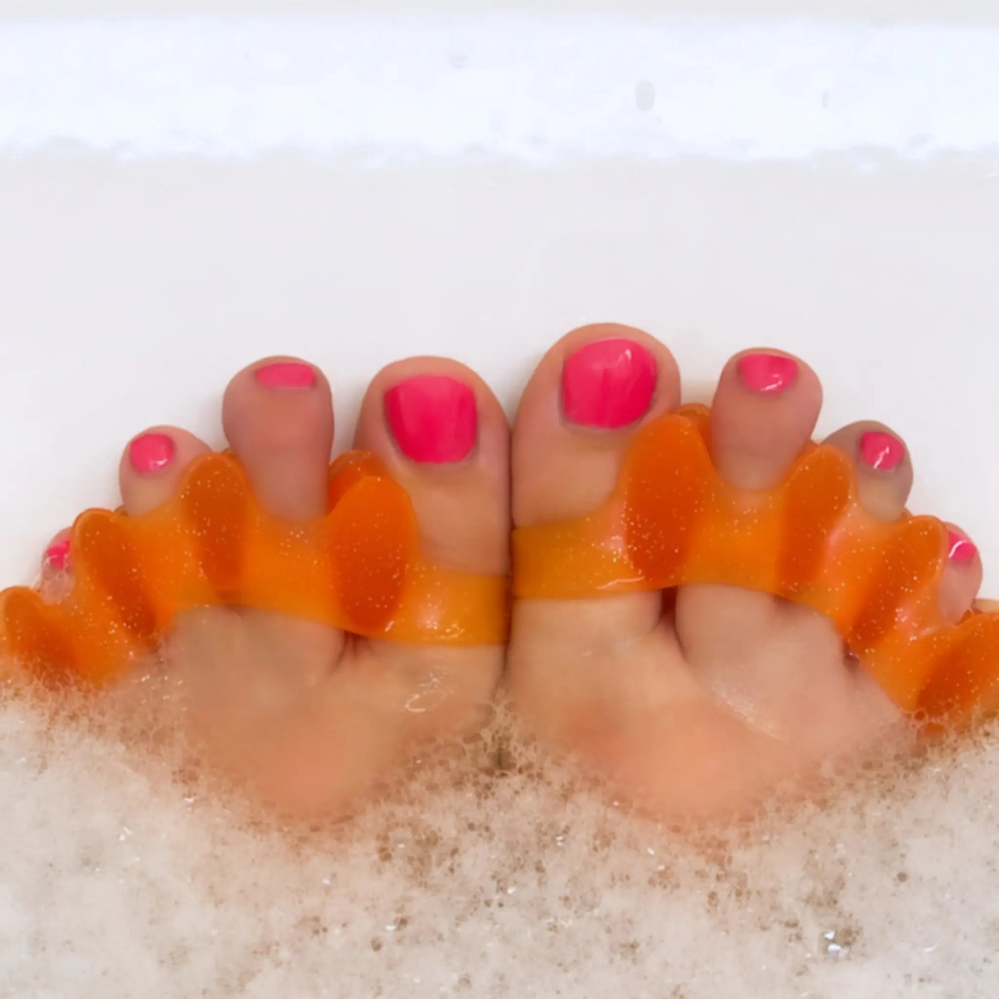 Someone wearing Tingle Toes toe separators in a bubble bath.