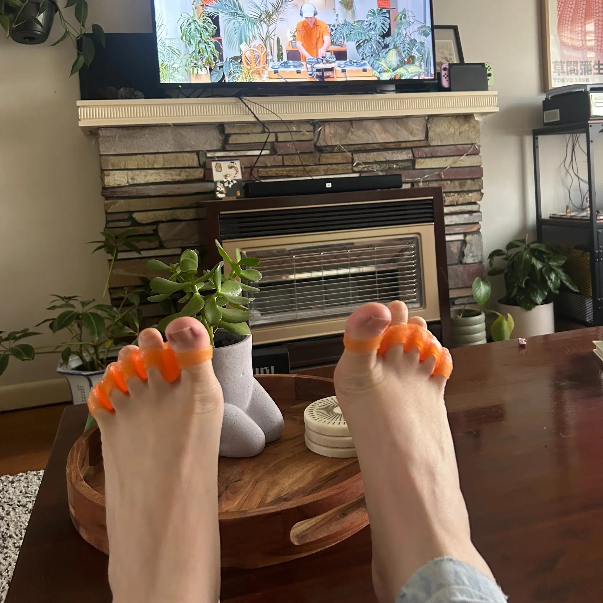 A person wearing Tingle Toes toe spacers on their couch watching TV.