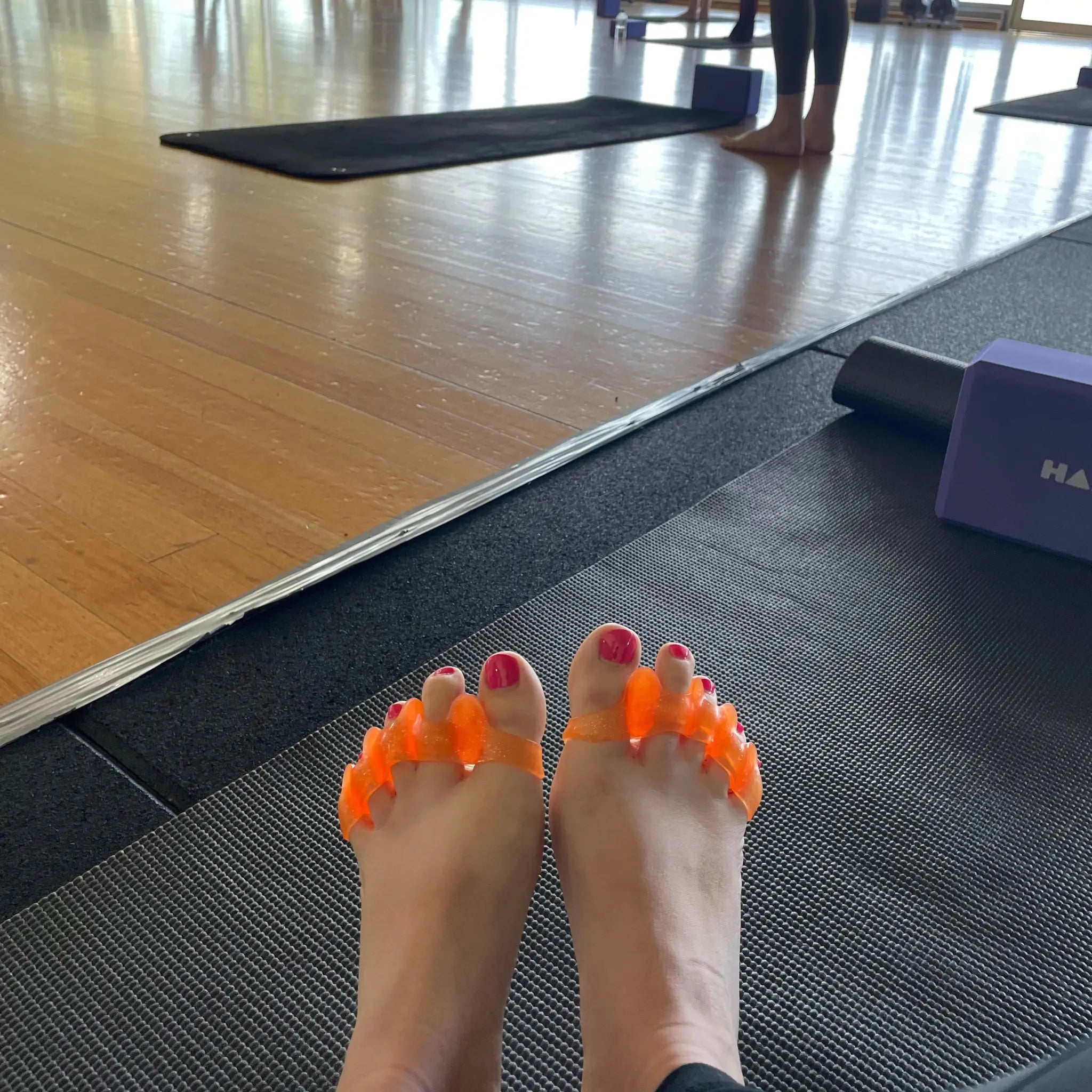 Wearing Tingle Toes toe spreaders on a yoga mat in a yoga studio.