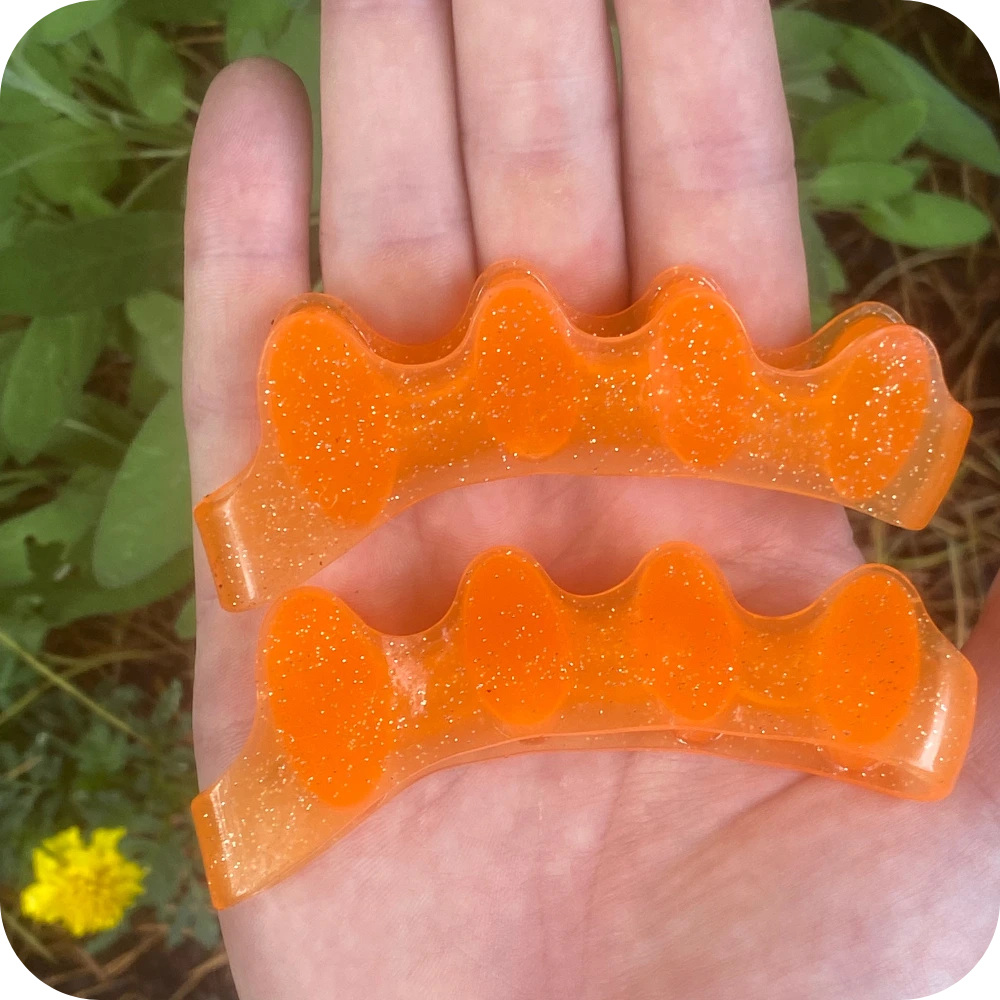 Close up of toe spreaders in an open palm over a garden bed