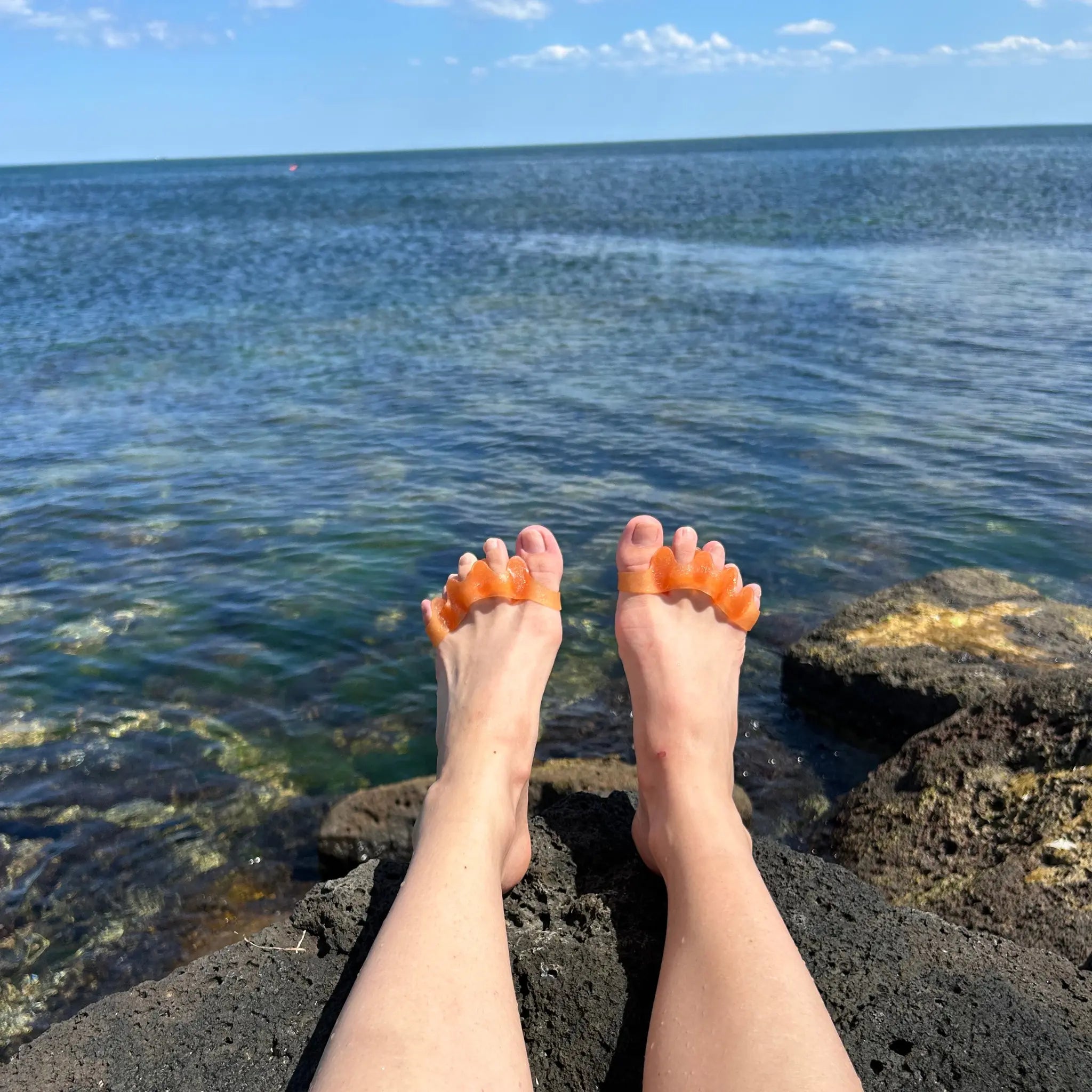 Someone wearing toe spreaders on a rock at the beach in front of the ocean and sky.